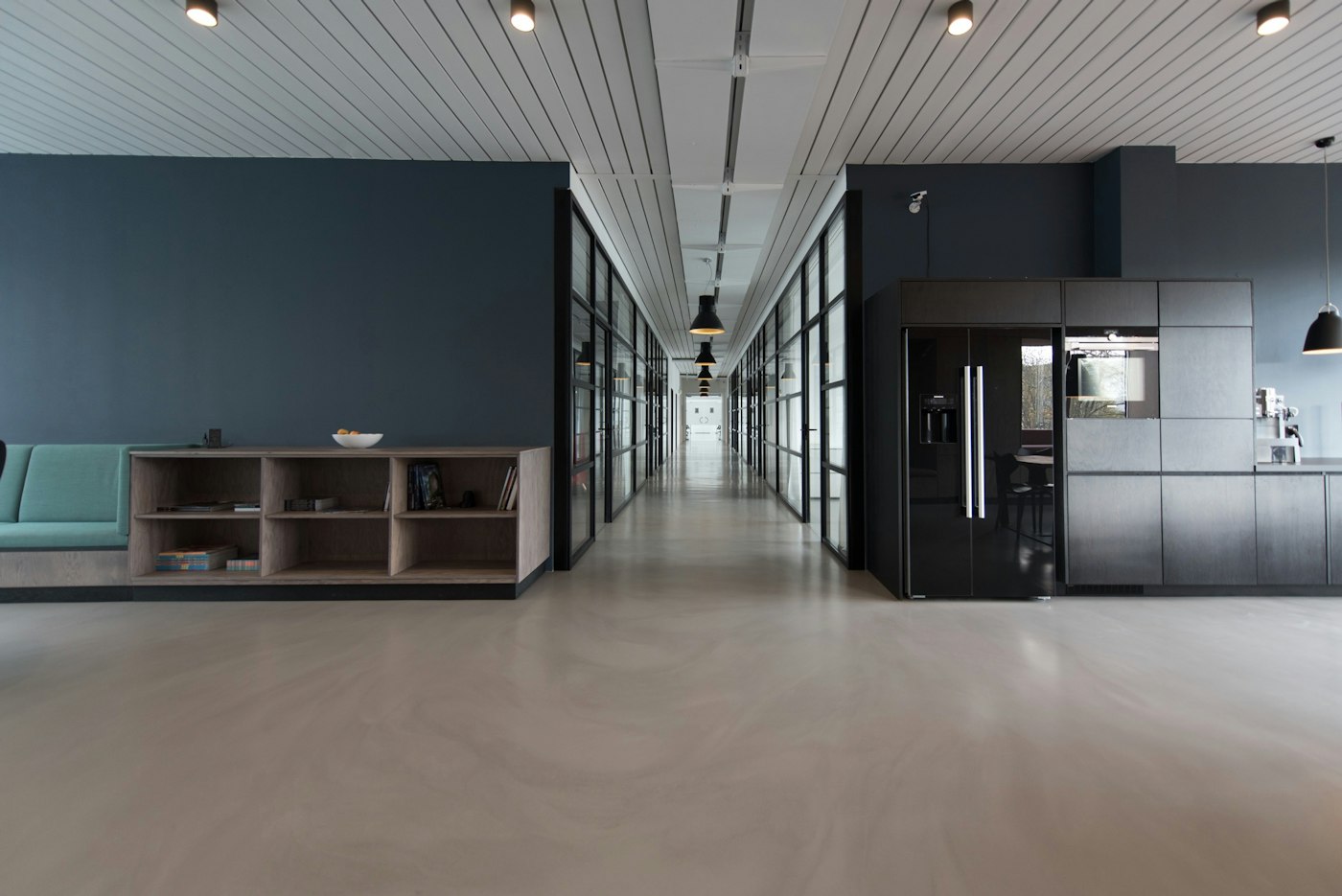 An office hallway with glass rooms, a kitchen, and a bench