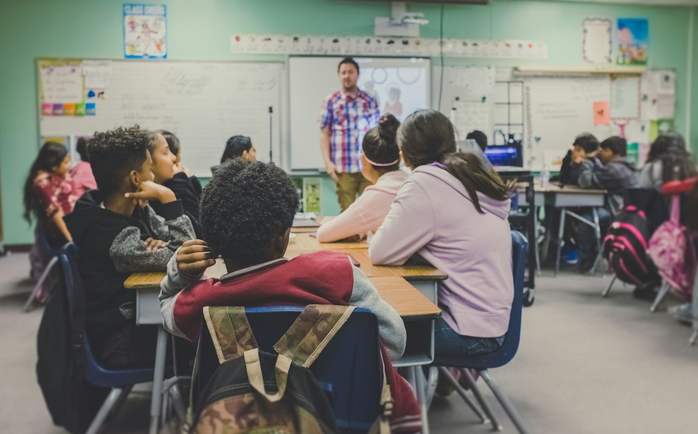 Students seated at desks while a teacher stands at the board